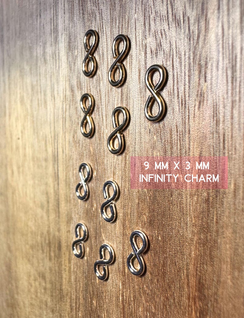May include: Ten gold-colored infinity charm pendants, each measuring 9 mm by 3 mm. The charms are arranged in a pattern on a wooden surface.