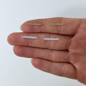 May include: Four small, delicate bar necklaces spelling "mama" in a cursive font. Two are gold-toned, and two are silver-toned. The necklaces are displayed on a person's hand against a white background.