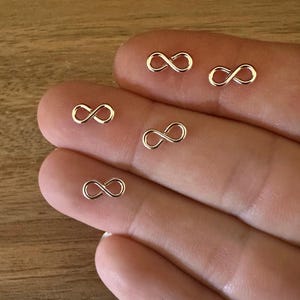 May include: Five silver infinity symbol charms on a hand. The charms are small and delicate.