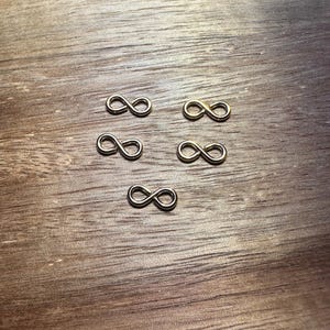 May include: Five silver infinity symbol charms on a wooden surface.