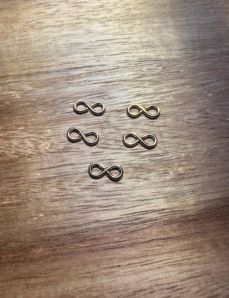 May include: Five silver infinity symbol charms on a wooden surface.