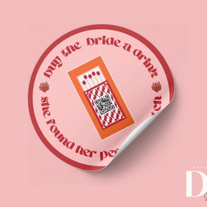 Op de afbeelding: Een ronde sticker in rood en wit met de tekst "buy the bride a drink" en een rood hart met vlammen. De sticker heeft een doosje lucifers met een QR-code. De tekst "Designed by DK Shop on Etsy" staat in de rechterbenedenhoek.