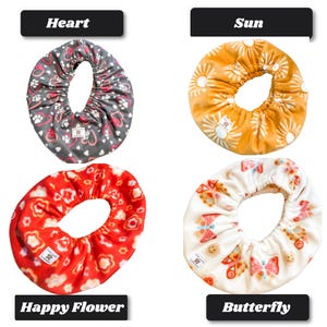 May include: Four circular fabric bowl covers with elastic edges. Top left: gray with pink hearts and white paw prints labeled Heart. Top right: mustard yellow with white suns labeled Sun. Bottom left: red with white flowers labeled Happy Flower. Bottom right: white with colorful butterflies labeled Butterfly.