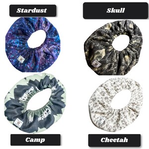 May include: Four circular fabric covers with elastic edges, each featuring a distinct pattern: a blue and purple galaxy print labeled Stardust, a black and gray skull print labeled Skull, a green and black camping scene labeled Camp, and a white and gray cheetah print labeled Cheetah.
