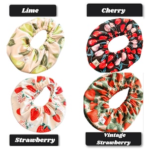 May include: Four circular fabric bowl covers with elastic edges. The top left features a lime pattern on a cream background. The top right shows a cherry print on black. The bottom left displays strawberries on cream, and the bottom right has a vintage strawberry pattern on green.