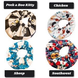 May include: Four circular fabric bowl covers with elastic edges. Top left features a black and white checkered pattern with cats and the text Peek a Boo Kitty. Top right shows chickens. Bottom left displays sheep. Bottom right features skulls and flowers.