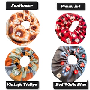 May include: Four circular fabric bowl covers with elastic edges. Top left features a sunflower print. Top right shows a red and black plaid pattern with white paw prints. Bottom left has a vintage tie-dye design. Bottom right displays a gray fabric with red, white, and blue star and heart motifs.