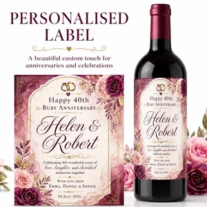 Op de afbeelding: Een wijnfles met een gepersonaliseerd etiket met bordeauxrode en roze bloemenillustraties, gouden accenten en twee in elkaar grijpende ringen. De tekst luidt Happy 40th Ruby Anniversary, Helen & Robert, 40 wonderful years, 20 July 2026.