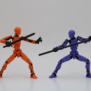 May include: Two articulated action figures, one orange and one purple, are posed in a fighting stance. The orange figure holds a black sword, while the purple figure holds a black staff.