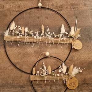 Könnte beinhalten: Zwei schwarze Metallreifen-Kränze, einer groß und einer klein, verziert mit Trockenblumen und Bindfaden. Jeder Kranz hat eine Holzperle zum Aufhängen und ein Etikett mit der Aufschrift "FOR YOU".
