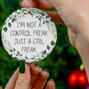 May include: A white ceramic Christmas ornament with green foliage around the edges. The ornament has the text "I'm not a control freak just a ctrl freak" on it.