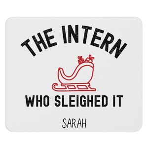 May include: White mousepad with the text "THE INTERN WHO SLEIGHED IT" in black, with a red sleigh graphic. The name "SARAH" is printed below the text in black.