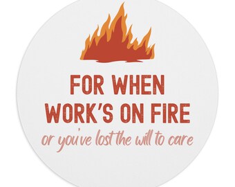 Może przedstawiać: Okrągła podkładka pod mysz w kolorze białym z grafiką ognia w kolorze czerwonym i pomarańczowym oraz tekstem "FOR WHEN WORK'S ON FIRE or you've lost the will to care".