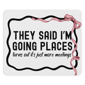Peut inclure: Un tapis de souris blanc avec une bordure noire et un ruban rose. Le texte sur le tapis de souris est "They said I'm going places turns out it's just more meetings."