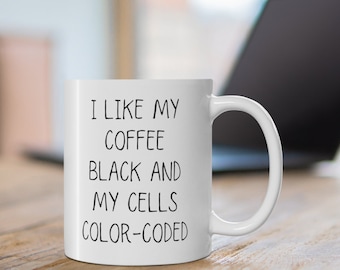 May include: White ceramic coffee mug with black text that reads "I like my coffee black and my cells colour-coded".