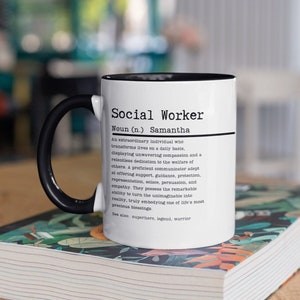 Könnte beinhalten: Eine weiße Keramiktasse mit schwarzem Henkel. Die Tasse hat einen schwarzen Rand und ein schwarz-weißes Design mit der Aufschrift "Social Worker Noun (n.) Samantha An extraordinary individual who transforms lives on a daily basis, displaying unwavering compassion and a relentless dedication to the welfare of others. A proficient communicator adept at offering support, guidance, protection, representation, solace, persuasion, and empathy. They possess the remarkable ability to turn the unimaginable into reality, truly embodying one of life's most precious blessings. See also: superhero, legend, warrior"