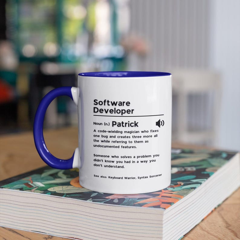 Pu&ograve; includere: Una tazza in ceramica bianca con bordo e manico blu. La tazza presenta una definizione di "Sviluppatore software" con il nome "Patrick" al posto della definizione. Il testo recita: "Sostantivo (n.) Patrick Un mago del codice che risolve un bug e ne crea altri tre, sempre riferendosi a loro come funzionalit&agrave; non documentate. Qualcuno che risolve un problema che non sapevi di avere in un modo che non capisci. Vedi anche: Guerriero della tastiera, Stregone della sintassi"