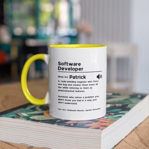 Pu&ograve; includere: Una tazza bianca con un bordo giallo. La tazza ha del testo nero che dice "Software Developer" e una definizione del termine. La definizione include il nome "Patrick".