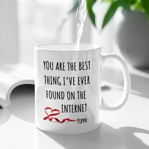 May include: White ceramic mug with black text that reads "You are the best thing I've ever found on the internet - Pippa". A red ribbon is tied in a heart shape on the mug.