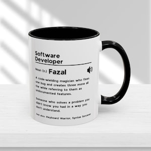 May include: White coffee mug with a black rim and handle. The mug has a black and white graphic that says "Software Developer" and defines the term as "A code-wielding magician who fixes one bug and creates three more all the while referring to them as undocumented features." The mug also says "Noun (n.) Fazal" and "See also: Keyboard Warrior, Syntax Sorcerer".