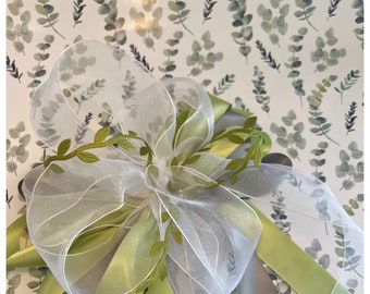 Puede incluir: Un lazo de cinta blanca transparente con hojas verdes sobre un fondo blanco con un patrón de acuarela verde.