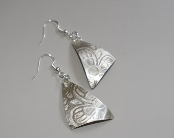 May include: A pair of silver earrings with a triangular shape and a textured floral design.