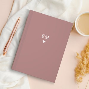 May include: A dusty rose colored journal with the initials "EM" and a small white heart printed on the front cover.