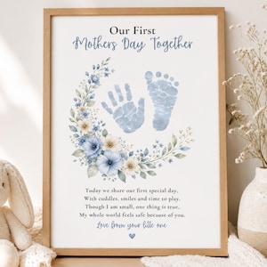May include: A framed print with the text "Our First Mothers Day Together." It features blue handprints and footprints, surrounded by a floral wreath with blue and white flowers. The print includes a poem and is displayed with a stuffed bunny and vase.