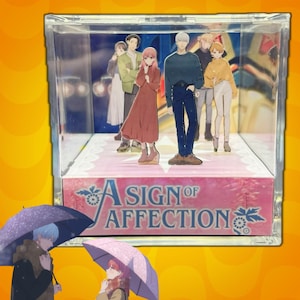 Può includere: Una vetrina trasparente in acrilico con personaggi in stile anime. I personaggi sono vestiti con vari abiti, con uno striscione rosa alla base che recita "A Sign of Affection". Due personaggi con ombrelli sono in primo piano.
