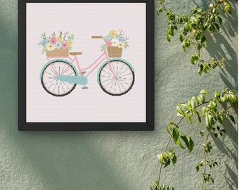 May include: A framed cross-stitch design of a light pink bicycle with two baskets filled with colorful flowers. The bicycle has light blue wheels and a black handlebar.