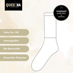 May include: A white sock with a black outline, featuring the text "QUEE XA inspiration of design". Additional text includes "Oeko-Tex 100", "Atmungsaktiv", "Bio-Baumwolle", and "Recycelter Polyester". A circular emblem reads "HANDMADE with love IN GERMANY".