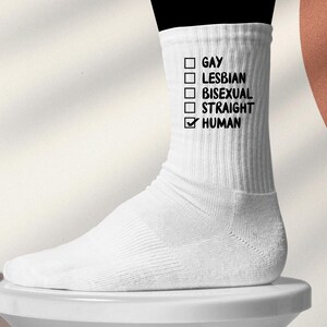 Könnte beinhalten: Weiße Socke mit den Wörtern "GAY", "LESBIAN", "BISEXUAL", "STRAIGHT" und "HUMAN" in Schwarz aufgedruckt. Das Wort "HUMAN" ist angekreuzt. Die Socke befindet sich auf einer weißen Oberfläche.