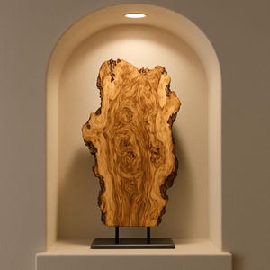 May include: A decorative wooden slab with a natural edge, displayed on a black metal stand. The wood features a rich, swirling grain pattern in shades of brown and tan, creating a unique, organic aesthetic. The piece is showcased in a recessed alcove.