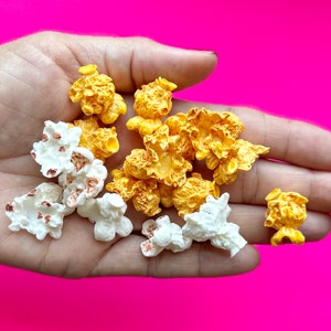 May include: A hand holding a variety of popcorn kernels, some are white and some are yellow.