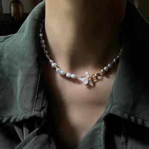 May include: A delicate pearl necklace with a gold flower charm. The necklace is made of small, white pearls and has a simple, elegant design.
