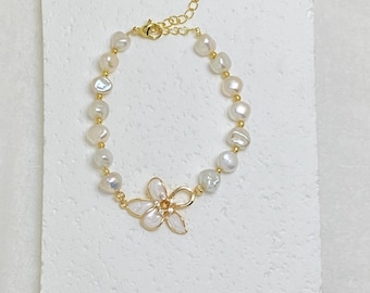 May include: A bracelet featuring white irregular freshwater pearls and small gold-toned beads. The centrepiece is a gold-toned metal flower charm with white petals and a small yellow stone in the centre. It includes a gold-toned chain extender.