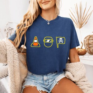 May include: Navy blue t-shirt featuring yellow outline graphics: a traffic cone, a welding mask, and a skull and crossbones flag. The tee is a relaxed fit, ideal for casual wear.