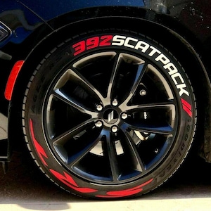 May include: A black car with a black tyre that has a white "392 SCATPACK" lettering with red accents.