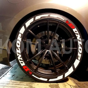 Puede incluir: Primer plano de un neum&aacute;tico de coche con una pegatina de letras de neum&aacute;tico blanca "UNILOP". La pegatina tiene una "D" roja y un c&iacute;rculo rojo con un punto blanco en el centro.