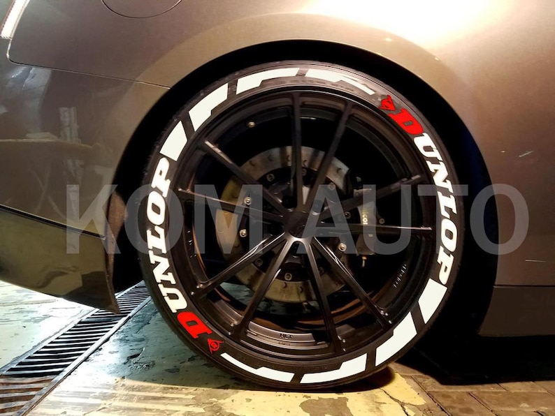 Puede incluir: Primer plano de un neum&aacute;tico de coche con una pegatina de letras de neum&aacute;tico blanca "UNILOP". La pegatina tiene una "D" roja y un c&iacute;rculo rojo con un punto blanco en el centro.