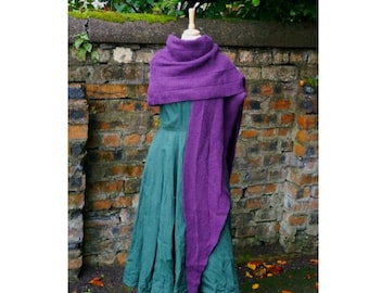 Può includere: Un scialle di maglia viola drappeggiato su un vestito verde. Lo scialle è lungo e fluido, con un collo a lupetto.