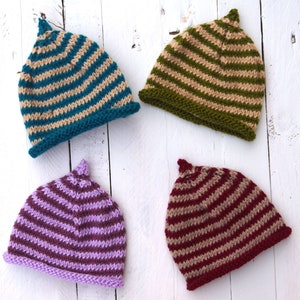 Può includere: Quattro berretti a maglia a righe in diversi colori: verde acqua e beige, verde e beige, viola e beige e bordeaux e beige.