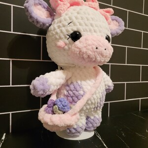 Finished Little Moo Cow amigurumi plushie made from beginner-friendly crochet pattern using chenille yarn, showcasing satchel and flower details.