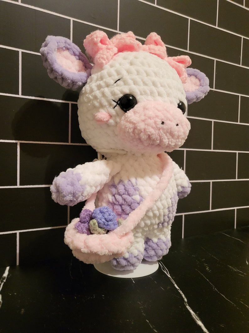 Finished Little Moo Cow amigurumi plushie made from beginner-friendly crochet pattern using chenille yarn, showcasing satchel and flower details.