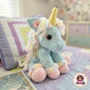 May include: A handmade, plush unicorn in pastel colors. The unicorn has a yellow horn, large black eyes, and pink and blue accents. It is sitting on a bed with a book titled "The Moon and the Unicorn" next to it. The unicorn is handmade.