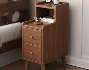 May include: A wooden nightstand with two drawers and a top shelf. The nightstand is brown with gold-colored knobs and has a small clock, a vase with flowers, and a book on top. The word "Wood" is in the bottom right corner.