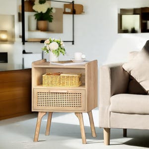May include: A light-colored wooden nightstand with a drawer and open shelf. The drawer features a woven rattan panel. A woven basket sits on the shelf, and a cup and saucer are on top. The nightstand has angled legs and a modern design.