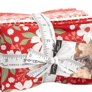 May include: A stack of red and white fabric squares with a floral pattern. The fabric is tied with a white ribbon with a measuring tape and the words "Moda Fabrics - Supplies" printed on it. The fabric is labeled with a white tag with the word "Moda" printed on it.
