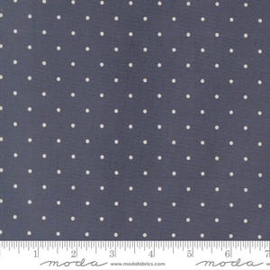 May include: A dark gray fabric featuring a repeating pattern of small, evenly spaced white polka dots. A white ruler is positioned along the bottom edge, showing a measurement scale in inches, with the text moda and www.modafabrics.com printed.