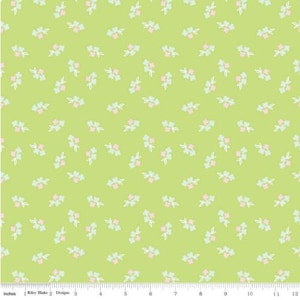 May include: A light green fabric with a repeating pattern of small floral clusters in pink and light blue, outlined in white. The fabric has a ruler along the bottom edge, with the text "Riley Blake Designs".